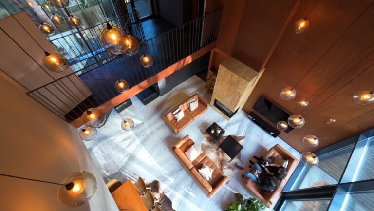 Ujęcie salonu z lotu drona FPV – nowoczesne wnętrze z wysokim sufitem i oświetleniem wiszącym, DroneFamily.